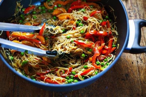 Stir fried Singapore Noodles in a pan with tongs.