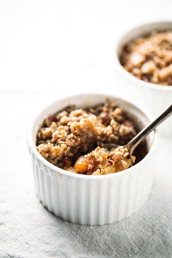 Coconut Oil Apple Crisp in a white baking dish with a wooden spoon.