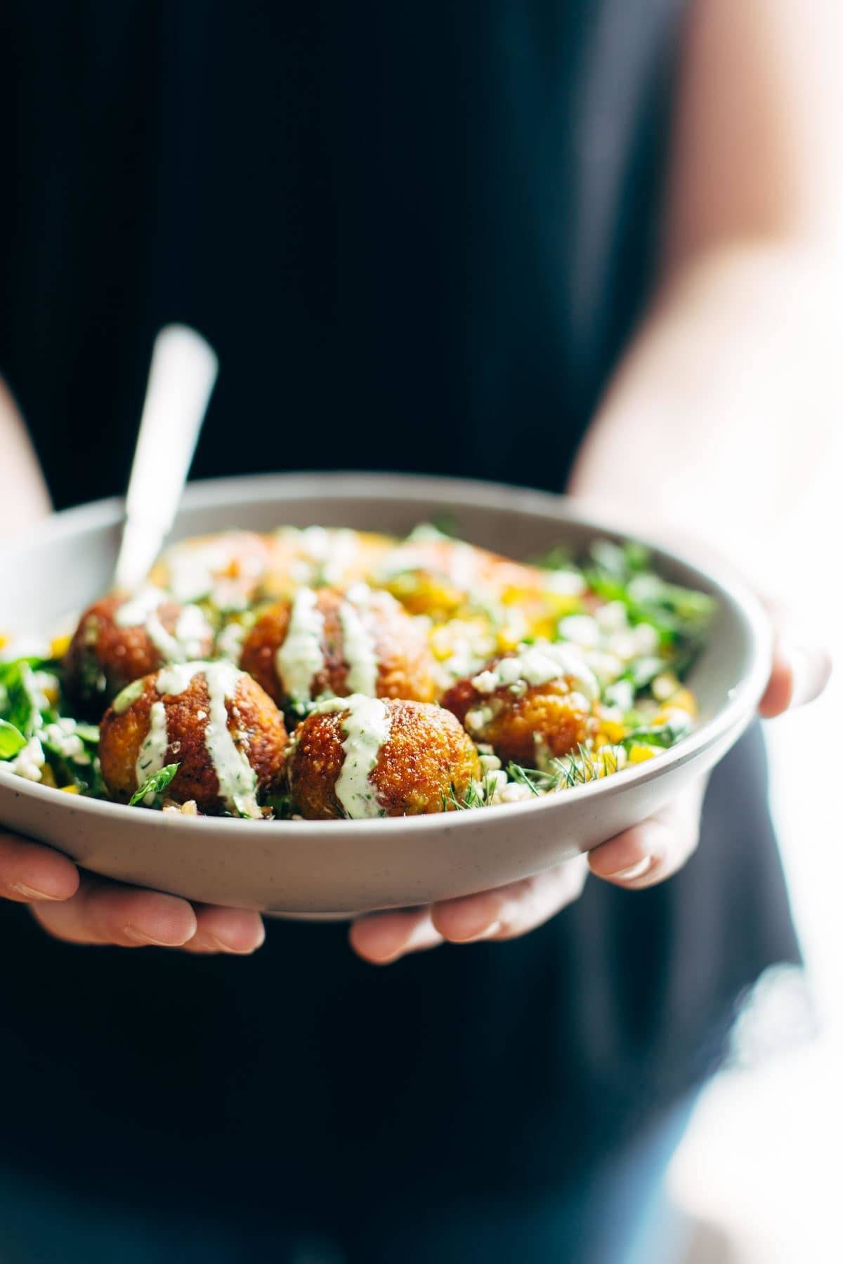 Hands holding Summer Bliss Bowls with Sweet Potato Falafel and Jalapeño Ranch.
