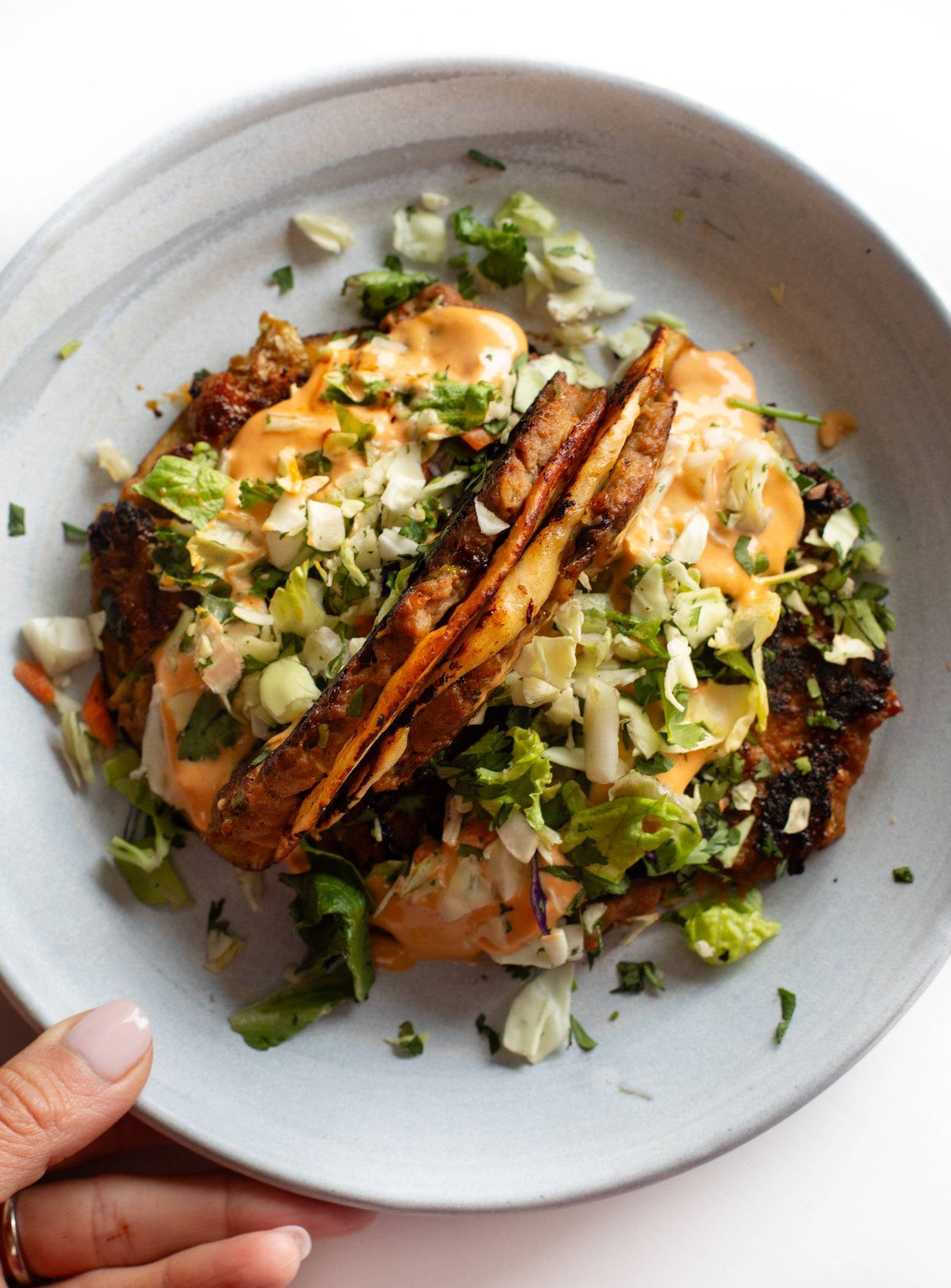 Two egg roll tacos on a plate topped with gochujang sauce.