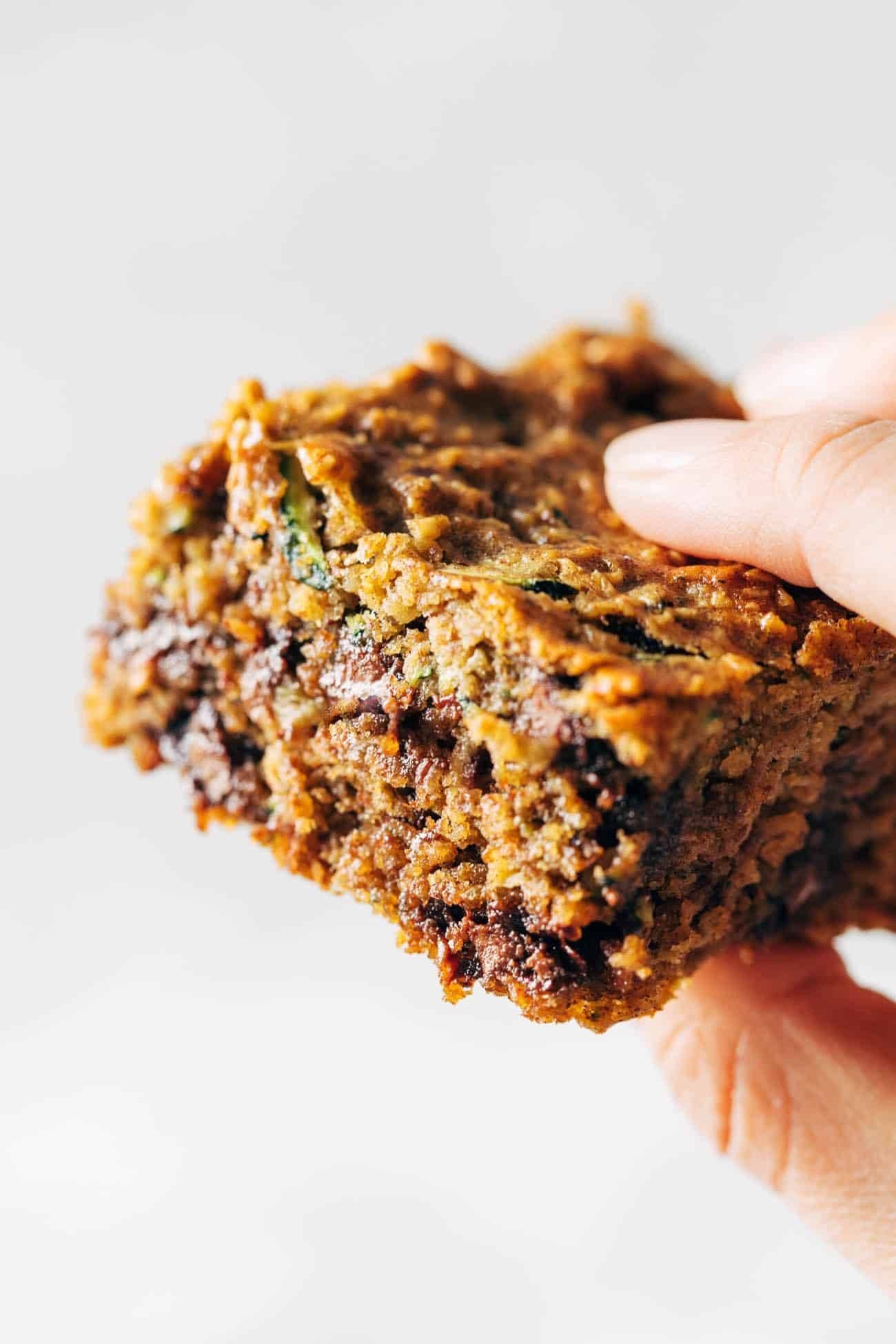 Close-up image of a white hand holding an almond butter chocolate chip zucchini bar. 
