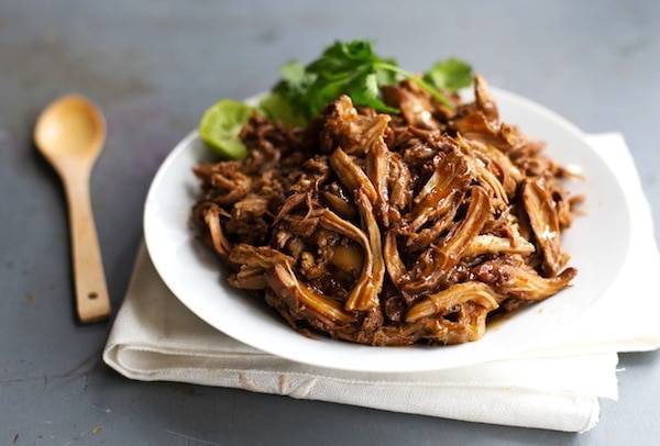 Honey Glazed Crockpot Chicken Adobo on a white plate with a wooden spoon.