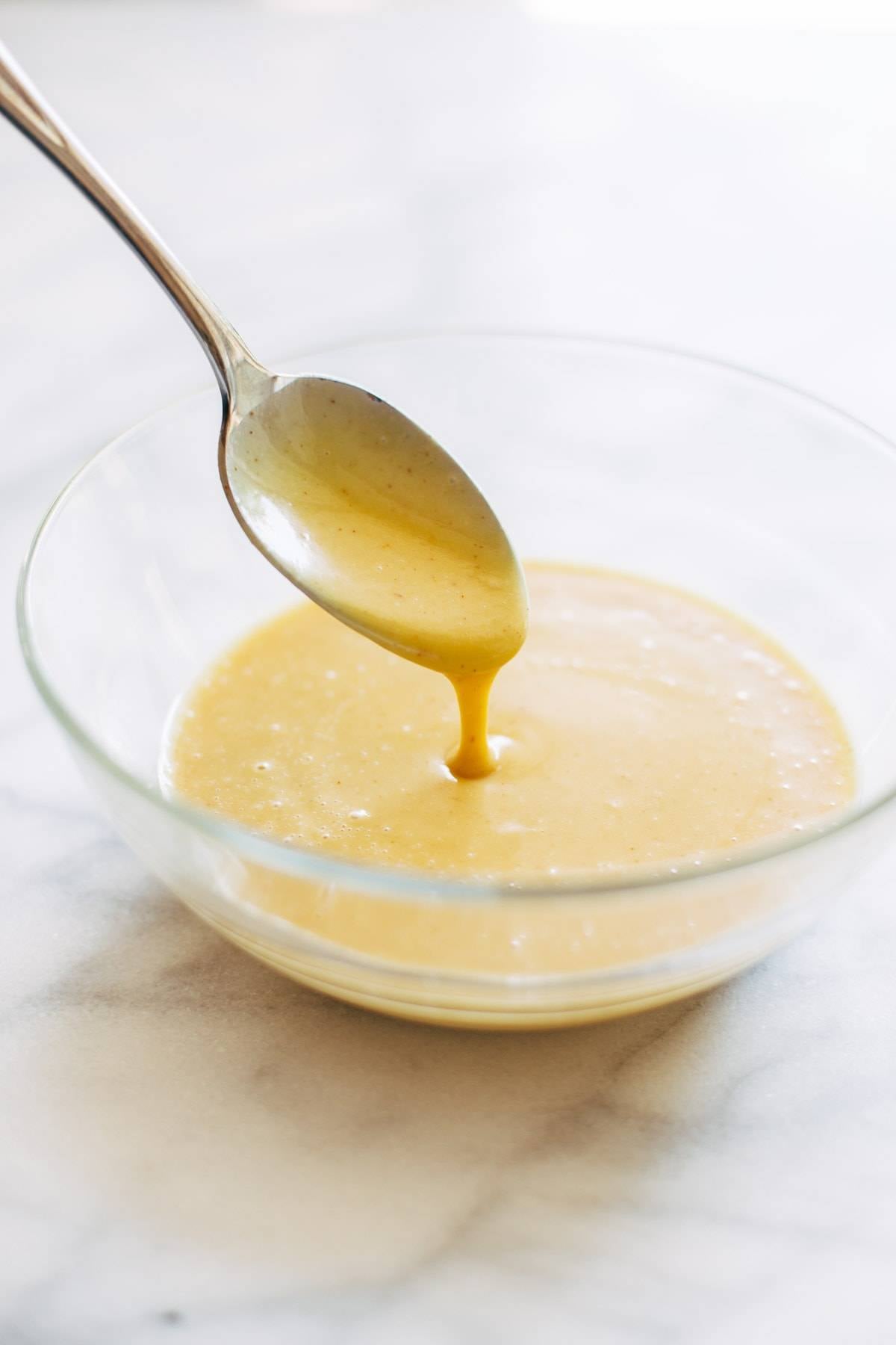 Spoon being dipped into bowl of honey mustard sauce.