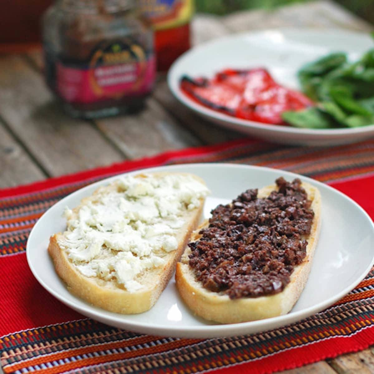 Assembly of a red pepper and goat cheese panini on a white plate.